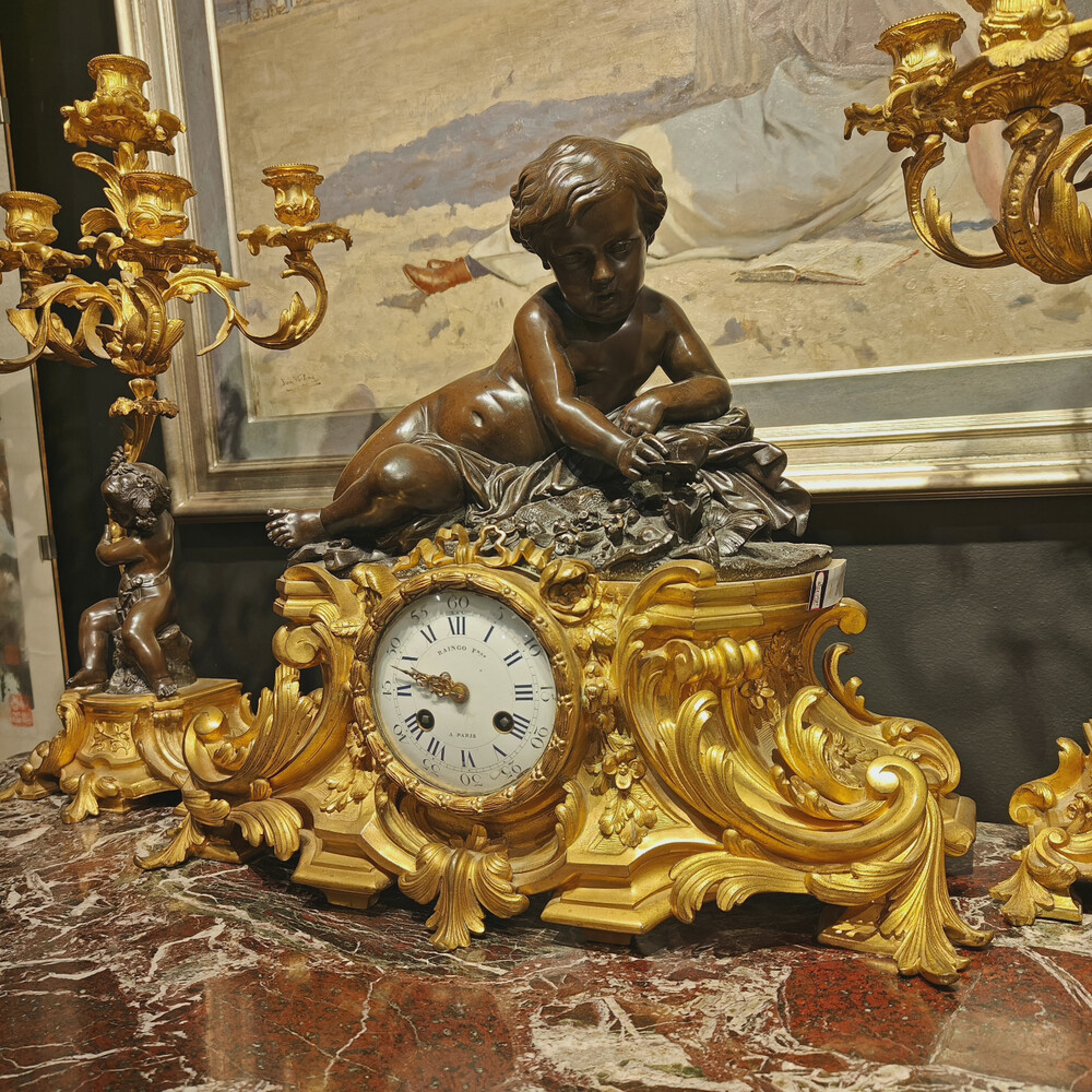 Belle garniture de cheminée trois pièces en bronze doré et patiné couronnée d'un enfant jouant avec un papillon. Travail Français du 19eme siècle   Cadran signé Raingo frères à Paris