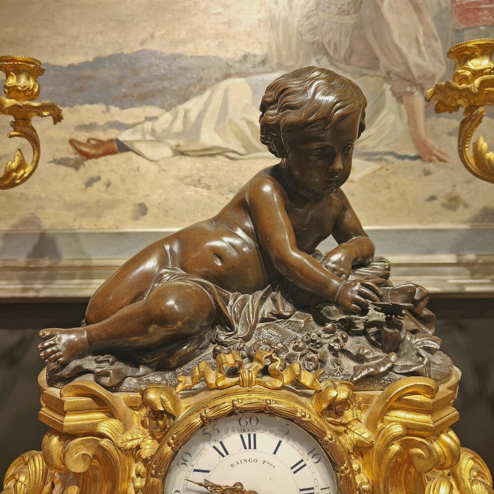 Belle garniture de cheminée trois pièces en bronze doré et patiné couronnée d'un enfant jouant avec un papillon. Travail Français du 19eme siècle   Cadran signé Raingo frères à Paris