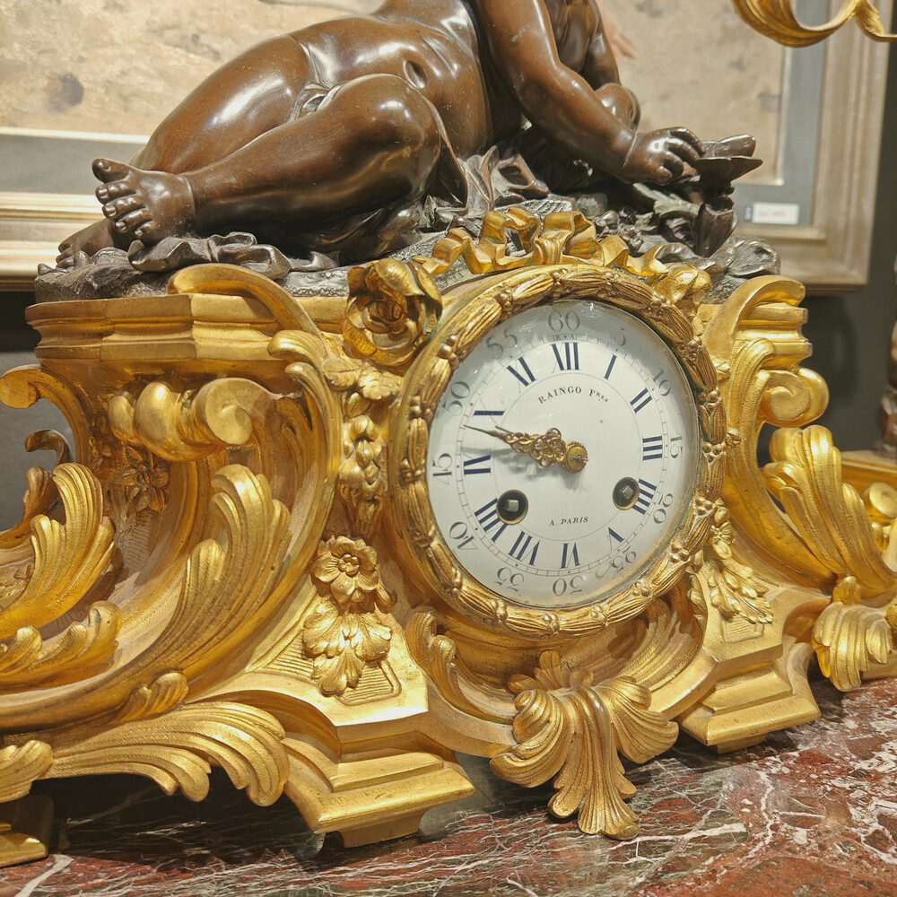 Belle garniture de cheminée trois pièces en bronze doré et patiné couronnée d'un enfant jouant avec un papillon. Travail Français du 19eme siècle   Cadran signé Raingo frères à Paris